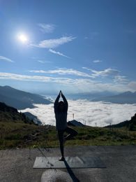 Selin in tree pose on a mountain meadow above a sea of cloud.