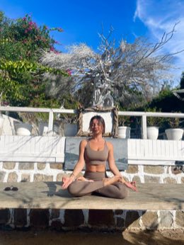Selin seated in meditation on a sunlit stone terrace.