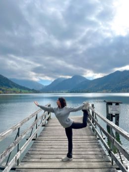Selin in dancer pose on a wooden jetty over a mountain lake.
