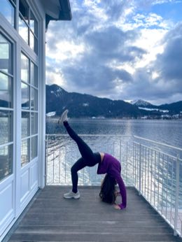 Selin in a standing split on a deck beside a snowy lake.