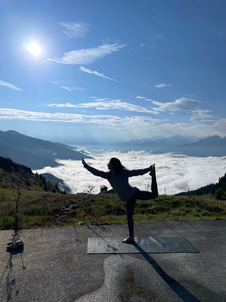 Selin in dancer pose in silhouette on a mountain ridge at sunrise, a sea of cloud below.